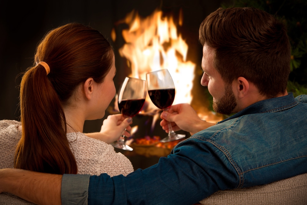 A couple enjoying a glass of wine by the fire, while enjoying one of the most romantic weekend getaways in michigan at our kalamazoo bed and breakfast